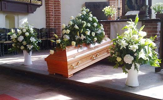 Eindrucksvolle Trauergebinde in weiss neben Sarg in Kirche